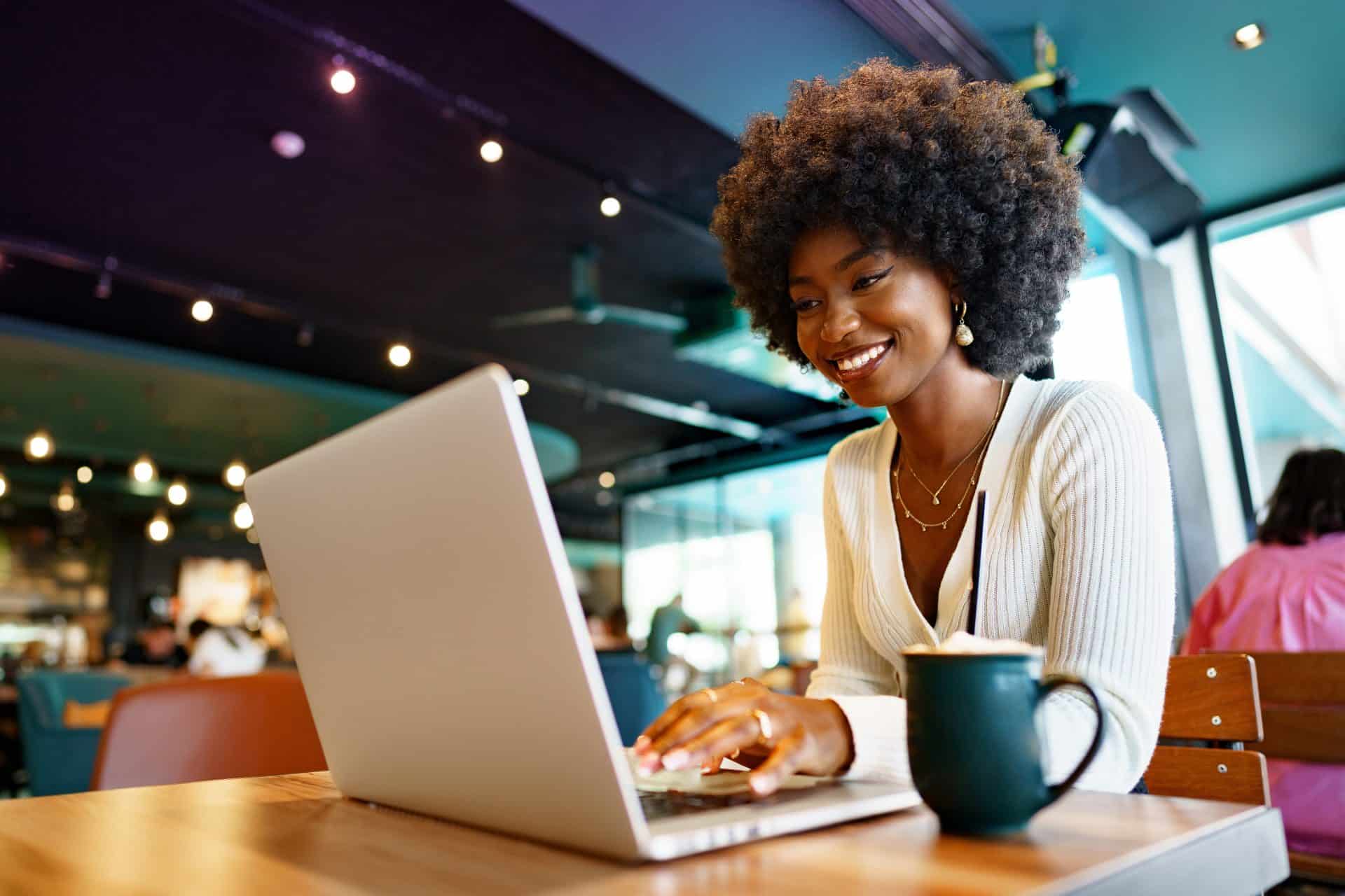 Smiling young african woman sitting with laptop in cafe, portrait reading business email