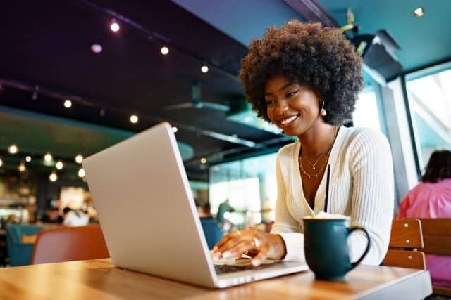Smiling young african woman sitting with laptop in cafe, portrait reading business email